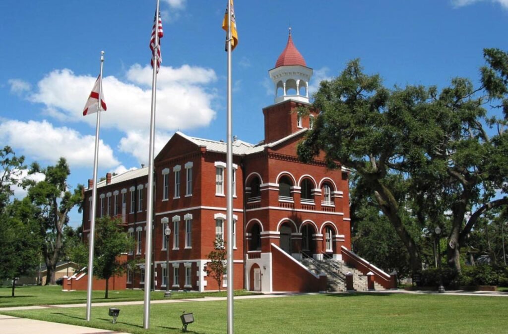 Historic courthouse building in Osceola County, Florida, featuring red brick architecture, a prominent clock tower, and surrounding flags, symbolizing the region's civic heritage.