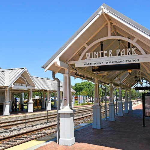 Winter Park train station with "WINTER PARK" sign, showcasing the platform and tracks in a bright, sunny setting, relevant to commercial cleaning services in Winter Park, FL.