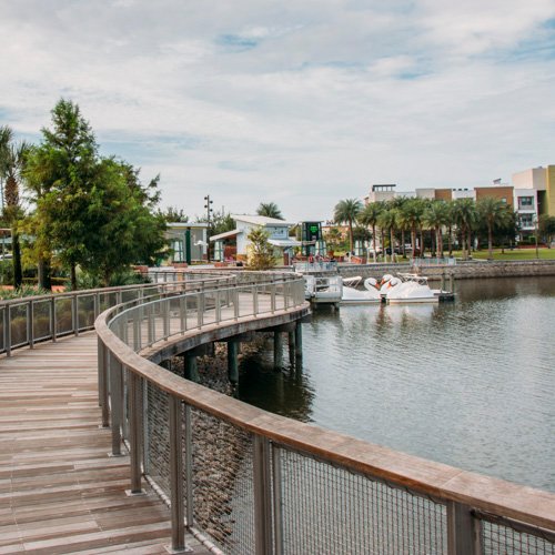 Scenic view of a boardwalk along a waterway in Oviedo, FL, featuring lush greenery and commercial buildings in the background, reflecting the community's vibrant environment.