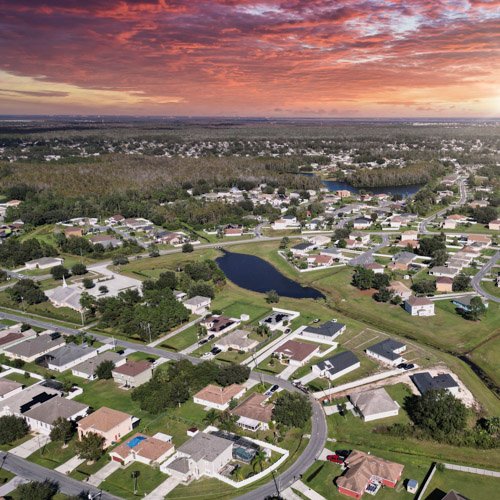 Aerial view of residential neighborhoods in Poinciana, FL, showcasing homes, green spaces, and a pond, emphasizing the community environment relevant to The Green Bucket's eco-friendly commercial cleaning services.