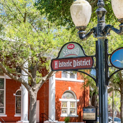 Old Sanford Historic District sign in front of brick building, surrounded by trees, representing the local heritage of Sanford, FL.